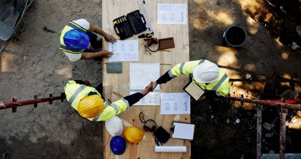 Overhead view of two construction professionals shaking hands over project plans